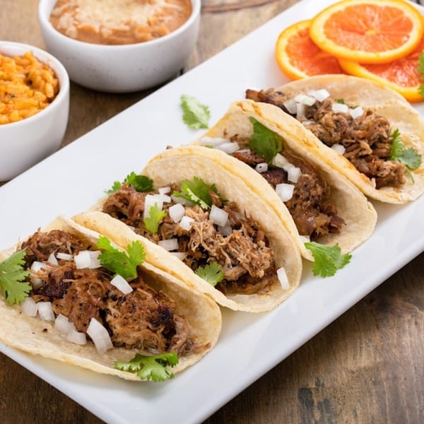 Four San Francisco Tacos & More carnitas tacos with cilantro and onions, with sides of rice and beans.